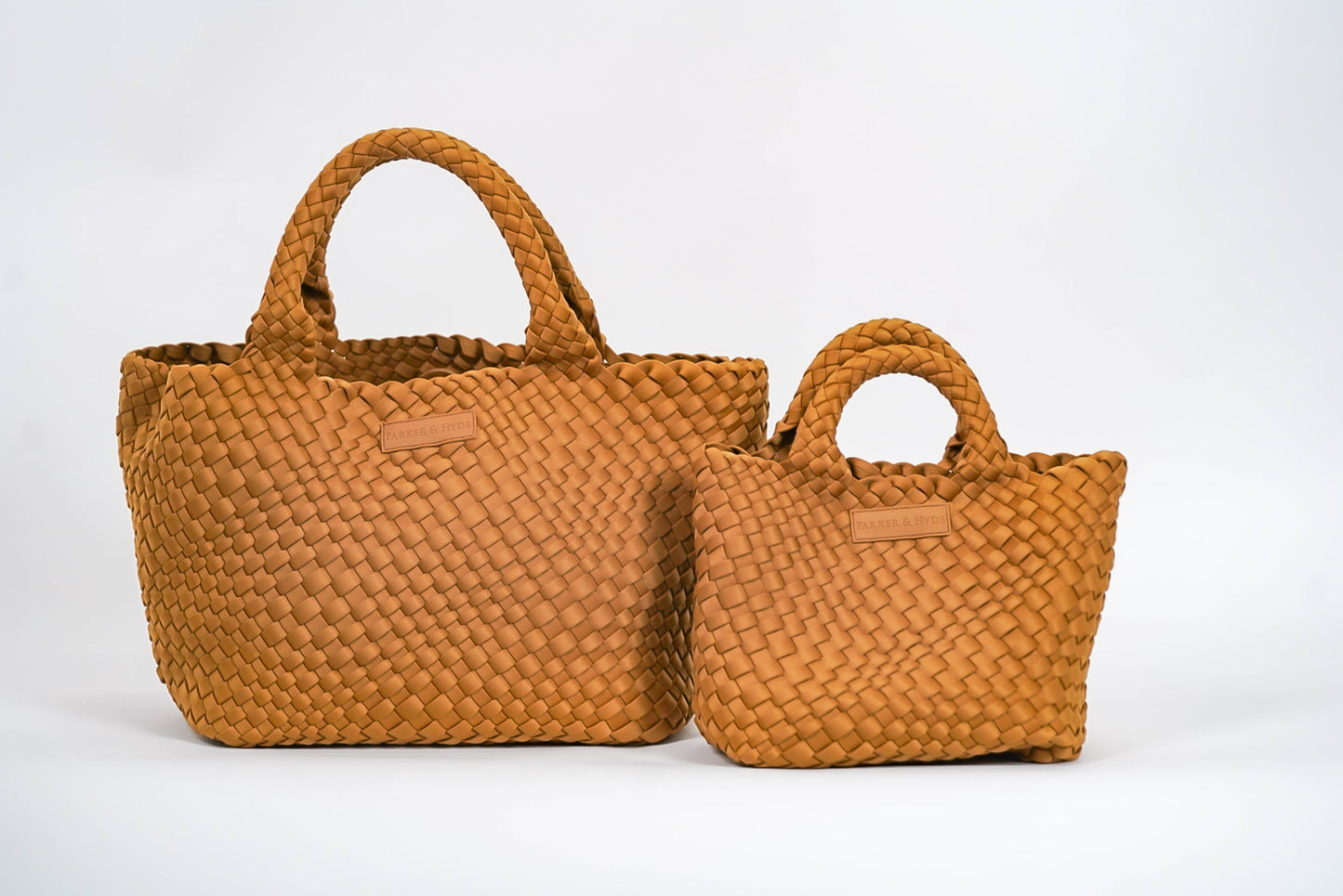 Two Parker & Hyde Classic Woven Tote bags in camel, each a different size, both featuring short handles and displayed side by side against a plain white background.