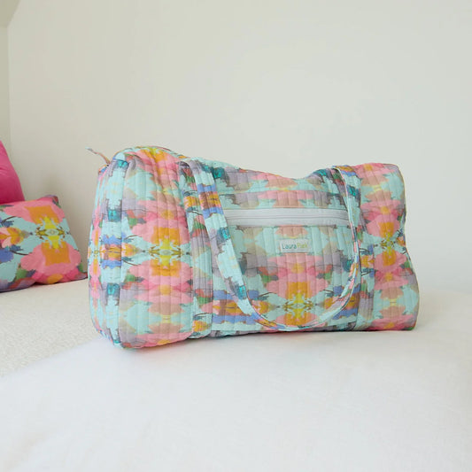 Laura Park Weekender Duffle in pastel geometric print, lying flat on white surface with handles visible