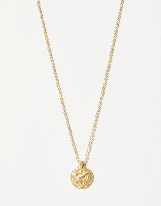 The Spartina Sea La Vie Always/Cardinal necklace by Spartina is a gold piece featuring a round coin pendant embossed with crossed arrows and a leaf, presented as an elegant remembrance gift against a plain white background.