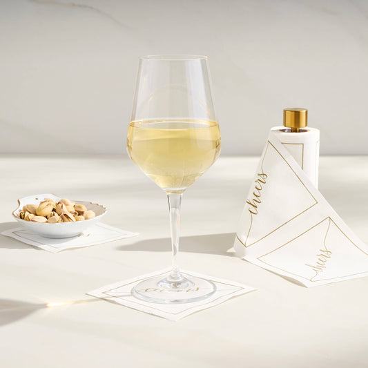 Table Theory gold cocktail napkin stand styled with white napkins, wine glass, and perfume bottle