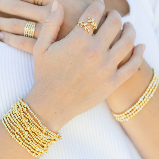 Multiple gold bead stretch bracelets stacked on wrist with rings, worn styling