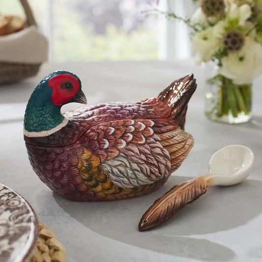 A Spode Woodland Pheasant Gravy Boat and Ladle from Spode, shaped like a colorful pheasant, sits on a table next to a bouquet of white flowers.