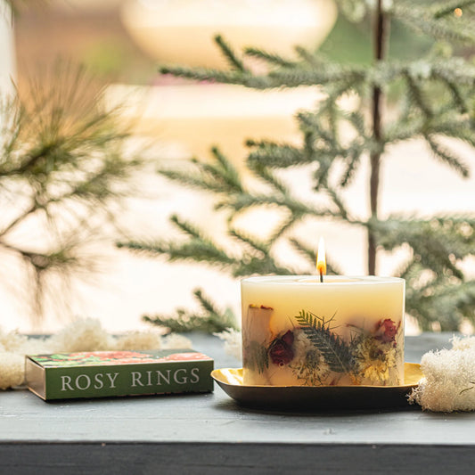 Rosy Rings botanical candle with dried botanicals on black candle plate, styled with evergreen sprigs and white decorative elements