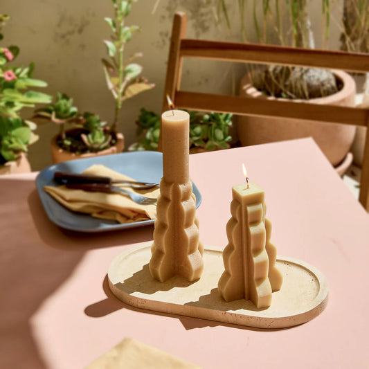 Two yuzu-colored Skeem tapers in ceramic holder on dining table with potted plants