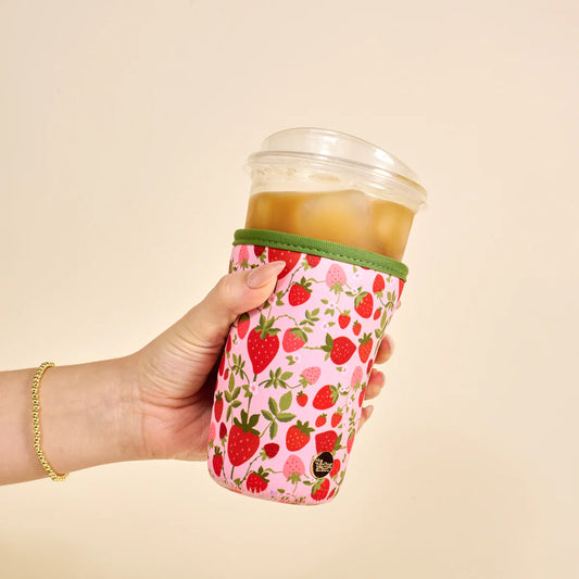 The Darling Effect Sip Savvy Drink Sleeve in pink with strawberry and floral pattern, worn on iced beverage held in hand