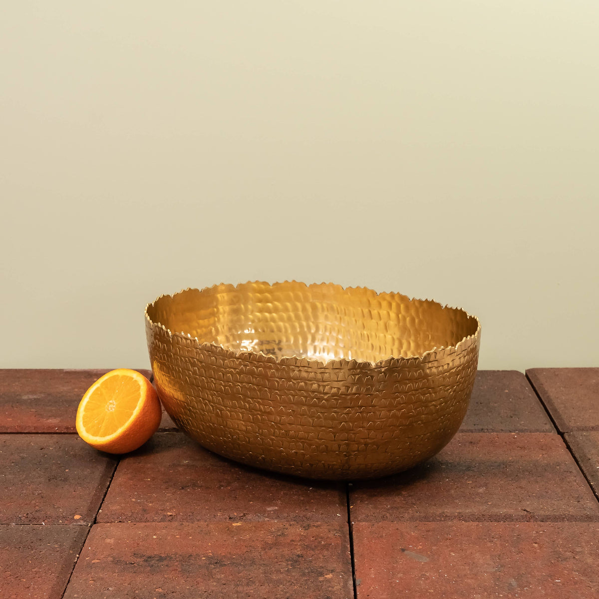 India Handicrafts Inc gold oval hammered bowl with orange slice for scale on wood surface