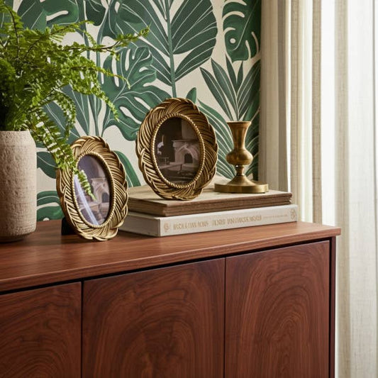 Gold polyresin feather oval frames arranged on wooden furniture with plant and decorative items