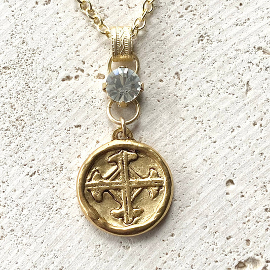 VB&CO Designs gold cross pendant necklace with faceted crystal stone on concrete background
