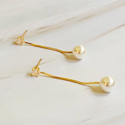 Ellison+Young Dangling Pearl Earrings pair on white marble, gold chain with crystal accent and cream pearl