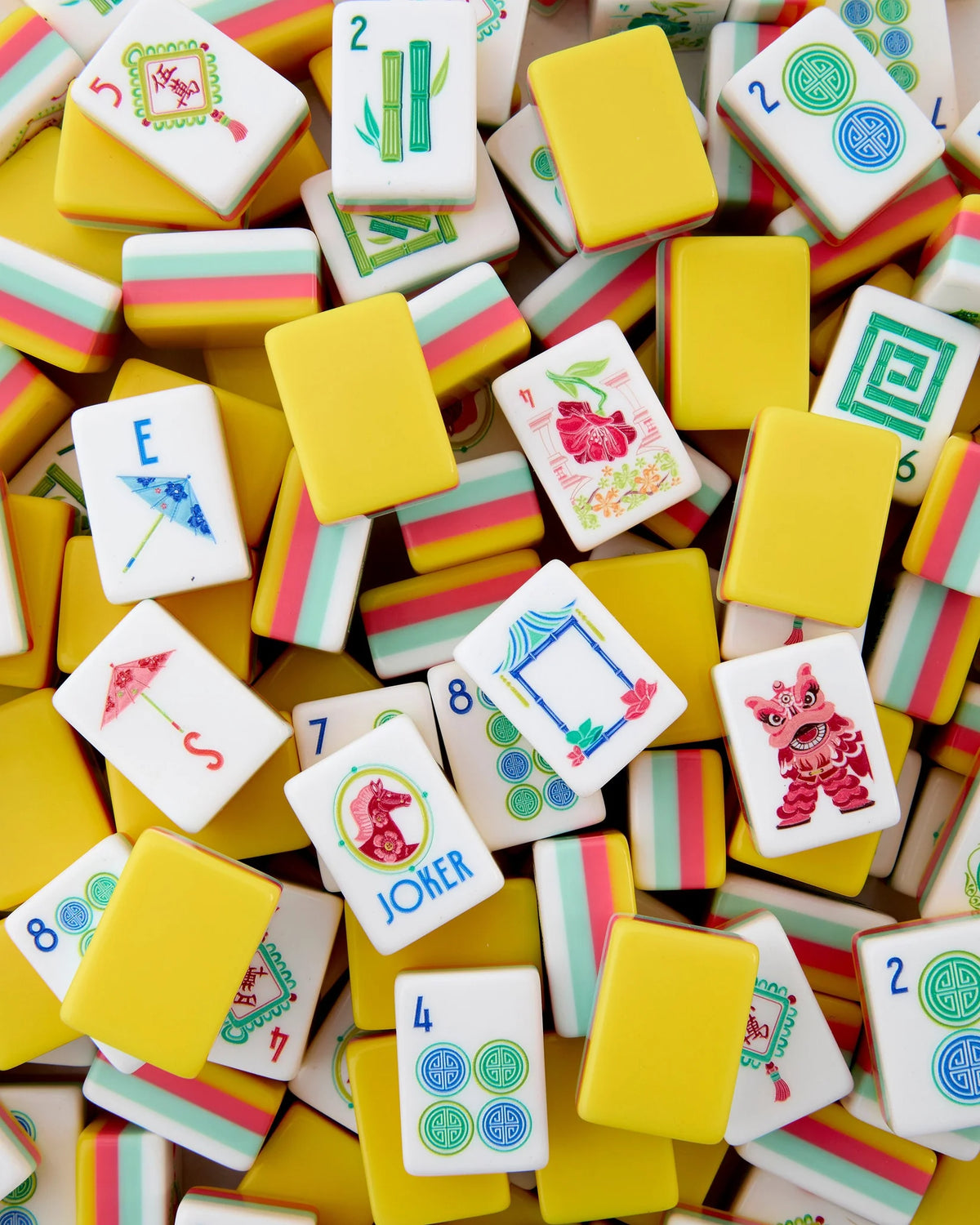 A vibrant stack of Oh My Mahjong Pippa Tiles features yellow backs and white fronts adorned with a variety of symbols, numbers, and illustrations—including dragons, circle patterns, and a playful “JOKER” tile—showcasing the lively design of Oh My Mahjong’s Pippa Tiles. This colorful mahjong set by Oh My Mahjong offers a modern twist to traditional gameplay with its contemporary tiles and dynamic details.
