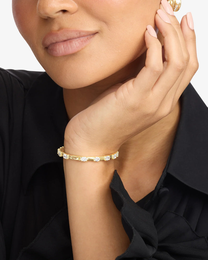 A person wearing a black blouse rests their chin on their hand, showing off the Melinda Maria She's On Point Station Cuff by Melinda Maria, a gold-plated bracelet with clear gemstones and manicured nails.