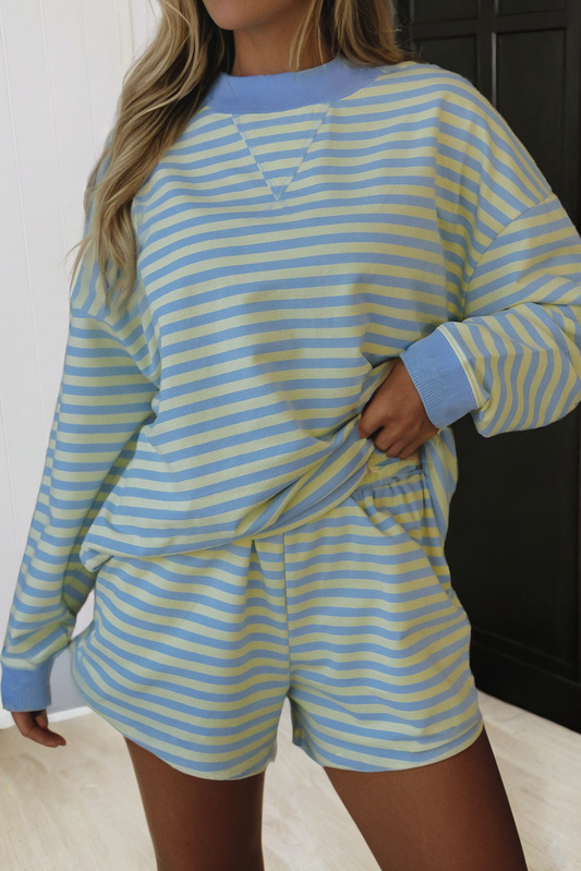 Wearing the LA Society LAS Stripe Color Block Pullover Shorts 2pcs Set, a person stands indoors with one hand on their hip, effortlessly showcasing the relaxed vibe and signature LA Society branding.