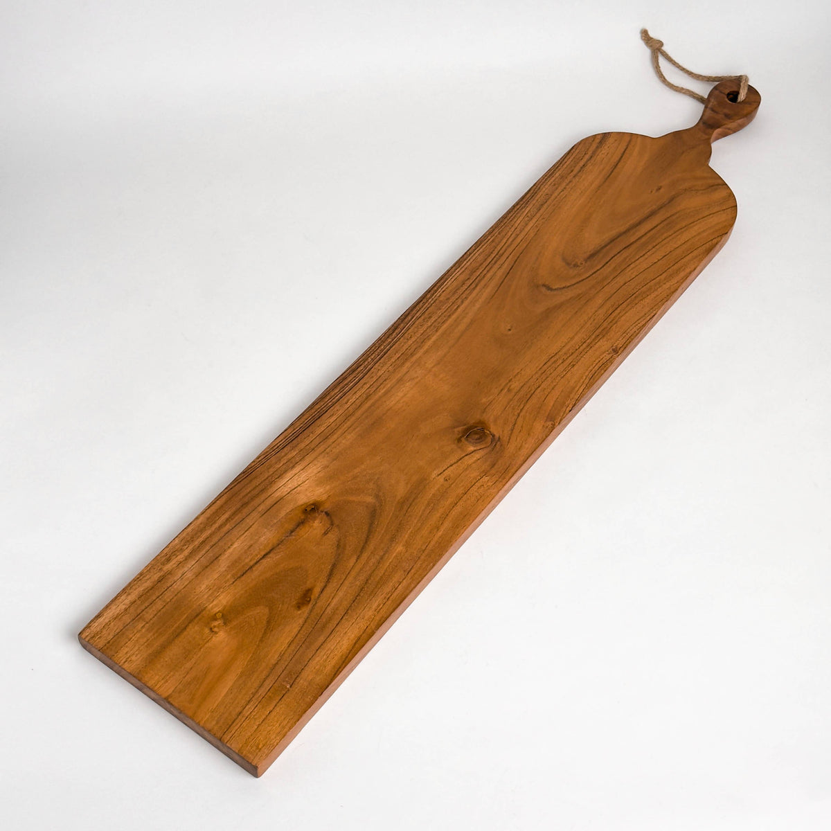India Handicrafts Inc slim acacia wood cutting board with rope handle, angled view showing grain and knots