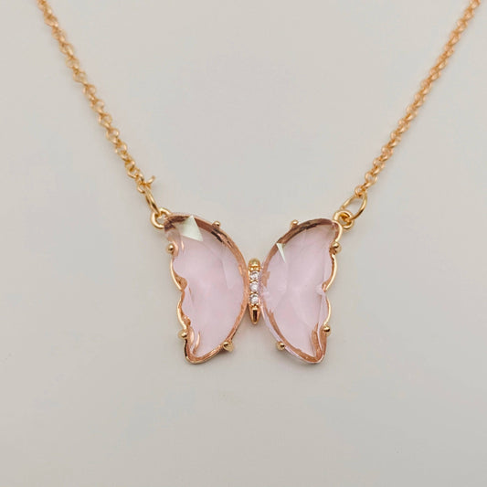 Introducing the Mio Queena - Multicolor Glass Butterfly Pendant Necklace by Mio Queena. This hypoallergenic necklace features a delicate butterfly pendant with translucent pale pink wings bordered in gold, accented by a row of tiny clear stones at the body. Set against a simple light background, this elegant piece beautifully combines charm and sophistication for everyday wear.