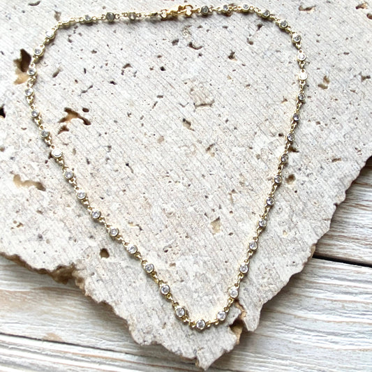 VB&CO Designs gold crystal layering necklace laid flat on textured fabric