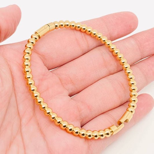 A hand holding the Mio Queena - 4mm Beads Gold Plated Stainless Steel Snap Bangle by Mio Queena is shown against a plain light background—an elegant, gold-plated accessory perfect for jewelry gifts.