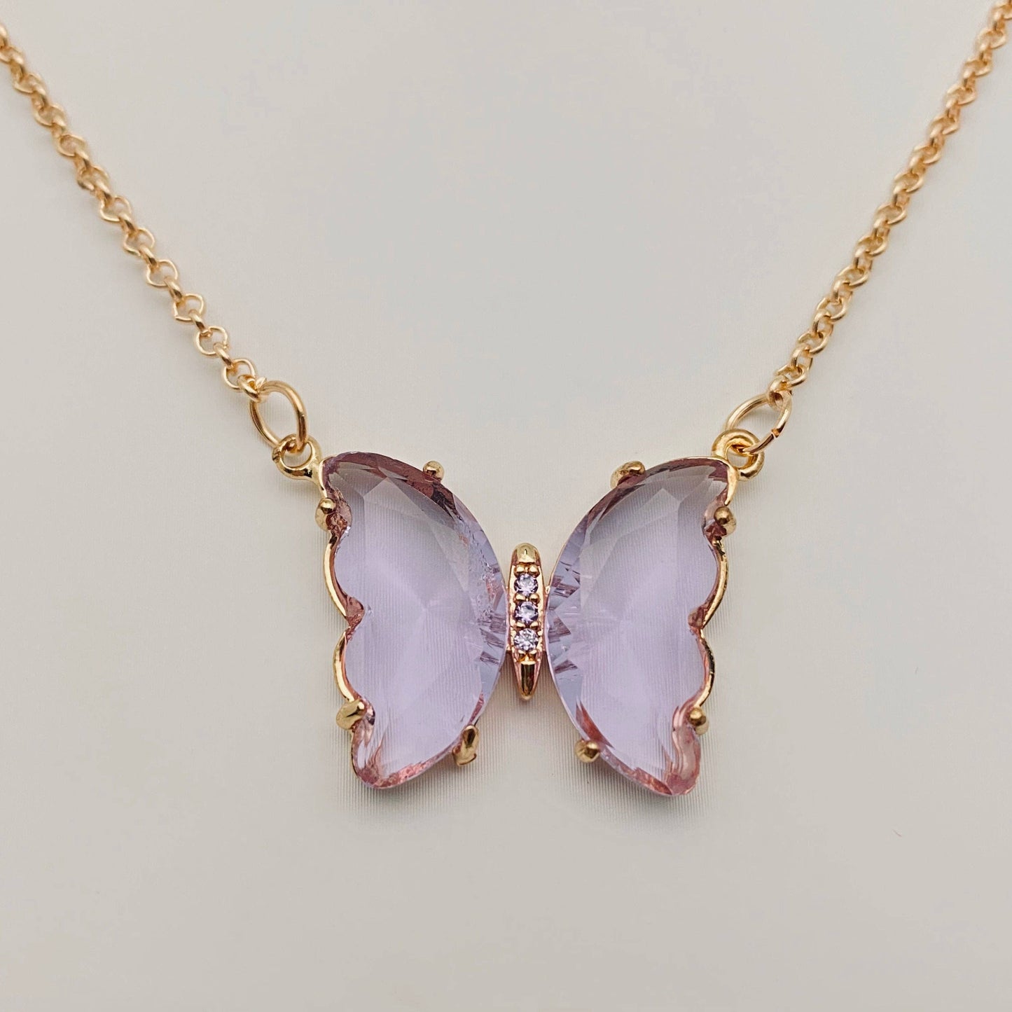 Introducing the Mio Queena - Multicolor Glass Butterfly Pendant Necklace by Mio Queena, featuring a delicate pendant with translucent light purple wings inspired by glass artistry and accented with small clear stones at the center. Hypoallergenic and perfect for everyday elegance.