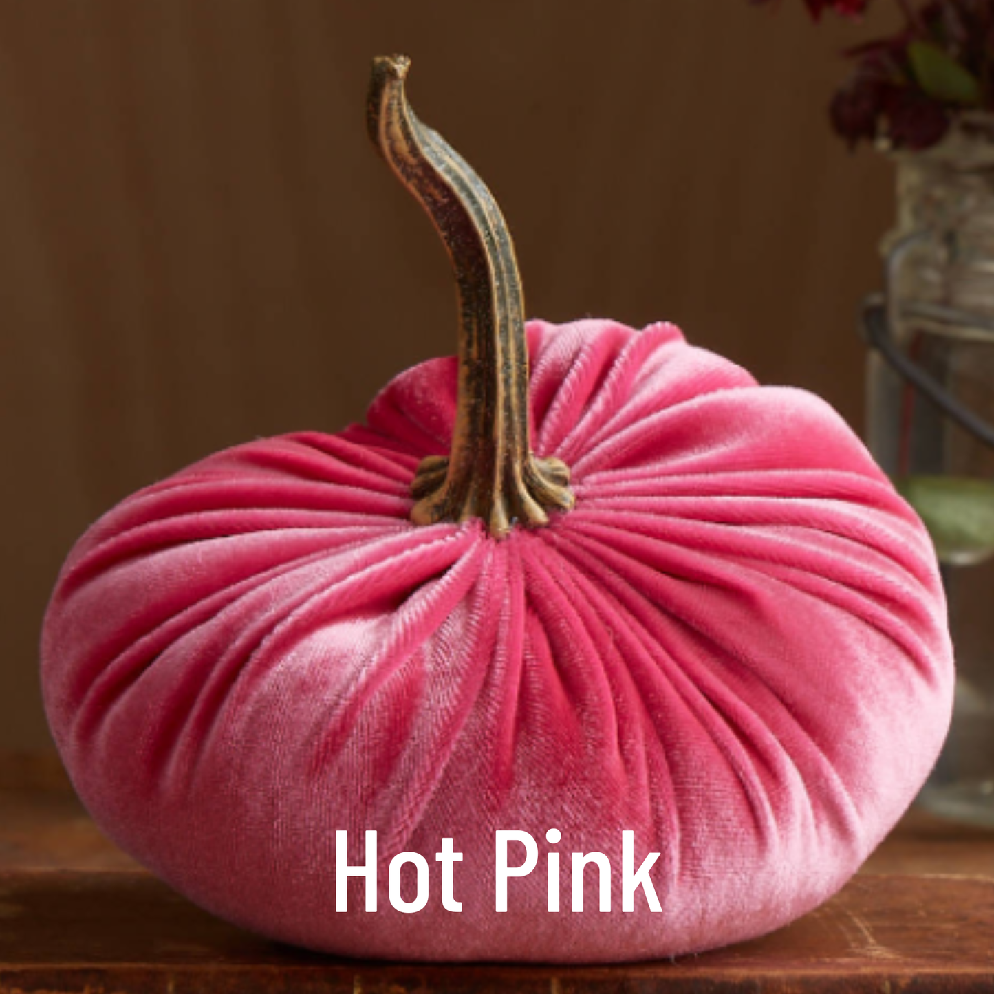 A large velvet pumpkin from Your Heart’s Content, in vibrant hot pink with a brown stem, sits on a wooden surface—making it a bold addition to your holiday mantel decor. The words “Hot Pink” are displayed in white text at the bottom of the image.