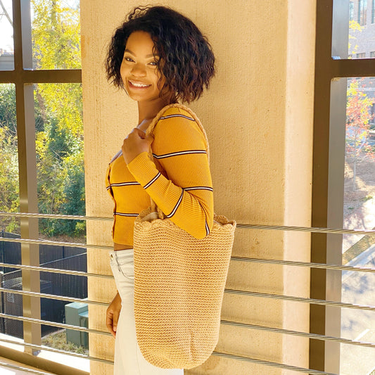 Woman wearing Ellison+Young Knitted Scalloped Edge Tote in natural straw, styled with mustard striped top