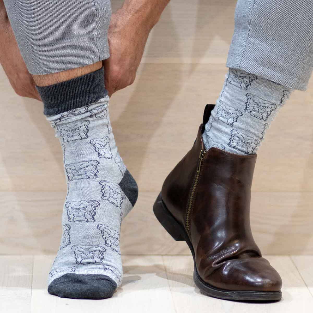 A person sporting The Royal Standard - Men’s Bulldog Face Socks, gray pants, and a single brown leather boot—while keeping their other foot bare—shows off distinctive Gameday flair that’s perfect for making a statement at an SEC matchup or cheering on Ole Miss in style.