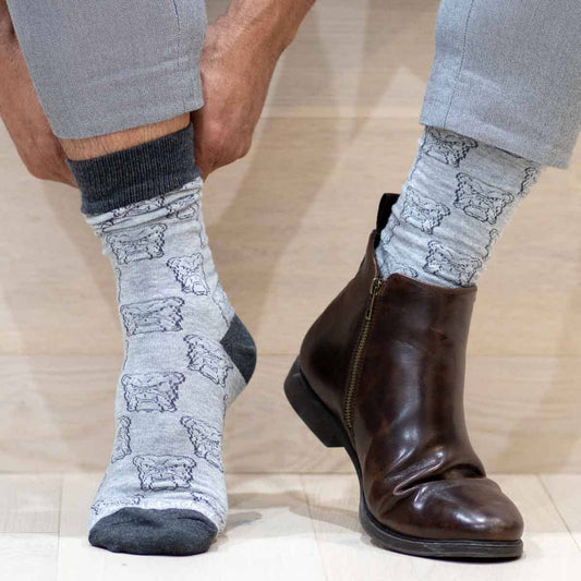 A person sporting The Royal Standard - Men’s Bulldog Face Socks, gray pants, and a single brown leather boot—while keeping their other foot bare—shows off distinctive Gameday flair that’s perfect for making a statement at an SEC matchup or cheering on Ole Miss in style.