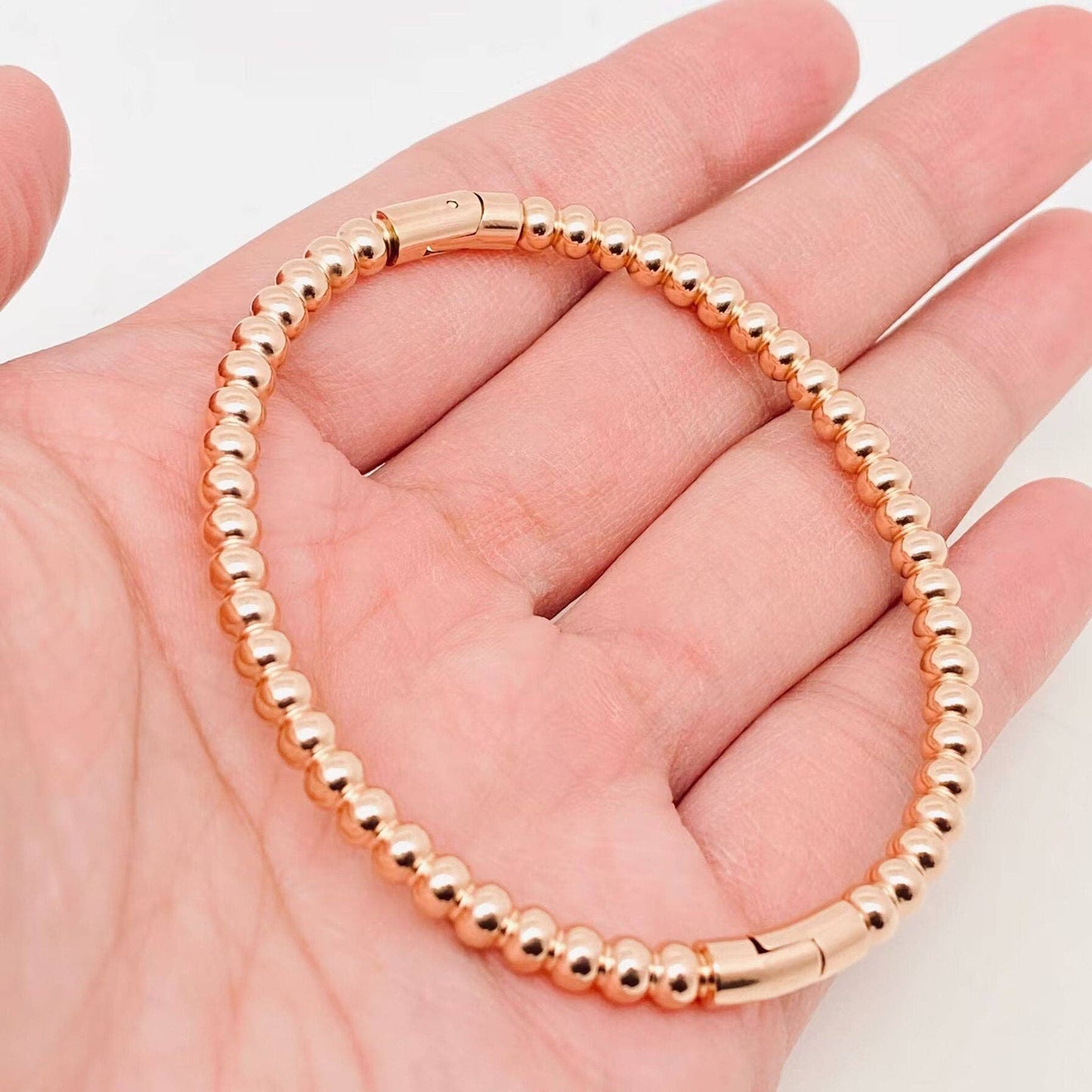 A hand displays the Mio Queena - 4mm Beads Gold Plated Stainless Steel Snap Bangle, featuring small round gold-plated beads and a secure snap clasp, set against a plain background—an elegant gift option from Mio Queena.