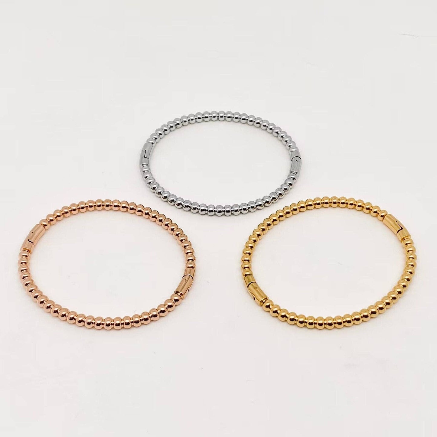 Three 4mm beaded metal snap bangles from Mio Queena—crafted with gold plated, rose gold, and silver stainless steel—are arranged in a triangular pattern on a plain white background, making the Mio Queena bangles ideal as elegant jewelry gifts.