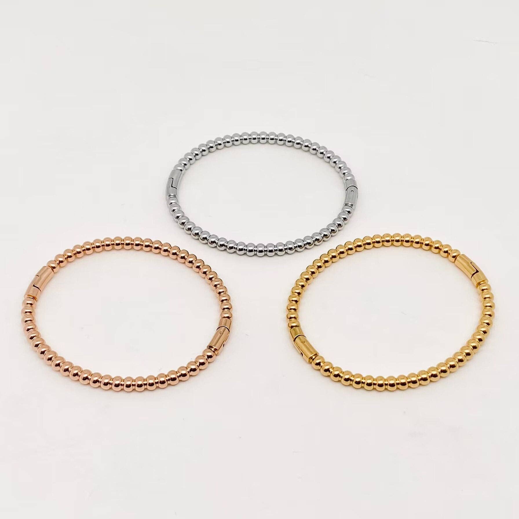 Three 4mm beaded metal snap bangles from Mio Queena—crafted with gold plated, rose gold, and silver stainless steel—are arranged in a triangular pattern on a plain white background, making the Mio Queena bangles ideal as elegant jewelry gifts.