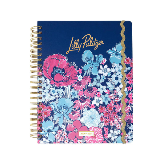 A spiral-bound Lilly Pulitzer by Lifeguard Press Jumbo 17 Month Agenda in the "In All Her Glory" design, featuring a navy blue hardcover adorned with a vibrant floral pattern, gold text, and a gold wavy stripe on the right. This eye-catching planner has a hardcover and includes a cover label that reads "2026 - 2027.