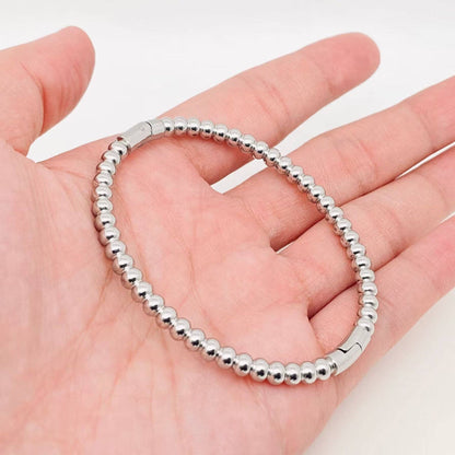 A hand holding the Mio Queena - 4mm Beads Gold Plated Stainless Steel Snap Bangle is displayed against a plain white background—an elegant accessory by Mio Queena that makes a thoughtful jewelry gift or pairs beautifully with your favorite stainless steel pieces.