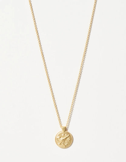 The Spartina Sea La Vie Always/Cardinal necklace by Spartina is a gold piece featuring a round coin pendant embossed with crossed arrows and a leaf, presented as an elegant remembrance gift against a plain white background.