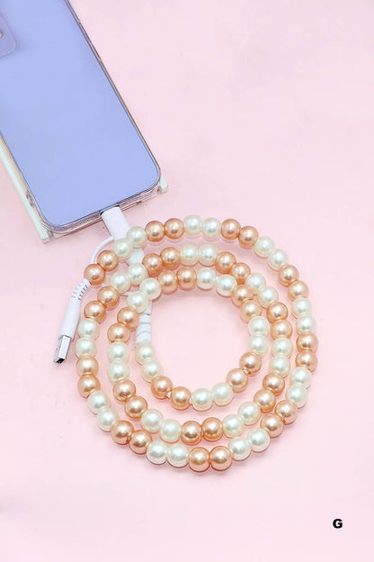 A lavender phone is paired with the 42POPS Beaded Dual USB Fast Charging Cable by 42POPS, decorated with alternating gold and white pearl-like beads and coiled on a light pink surface.