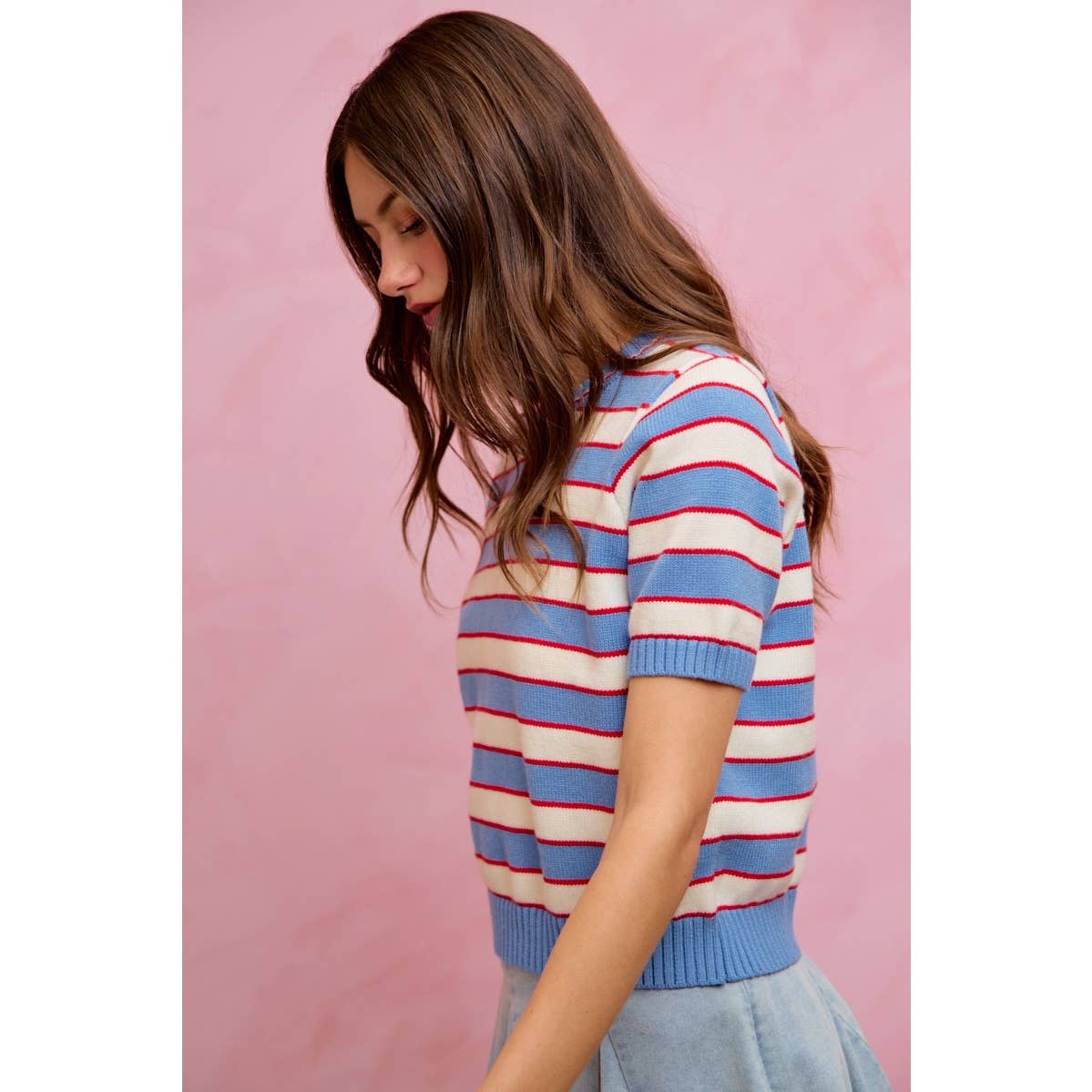 A woman with long brown hair stands in profile against a pink background wearing the So Me STRIPE KNIT CREW NECK SHORT SLEEVES SWEATER TOP.