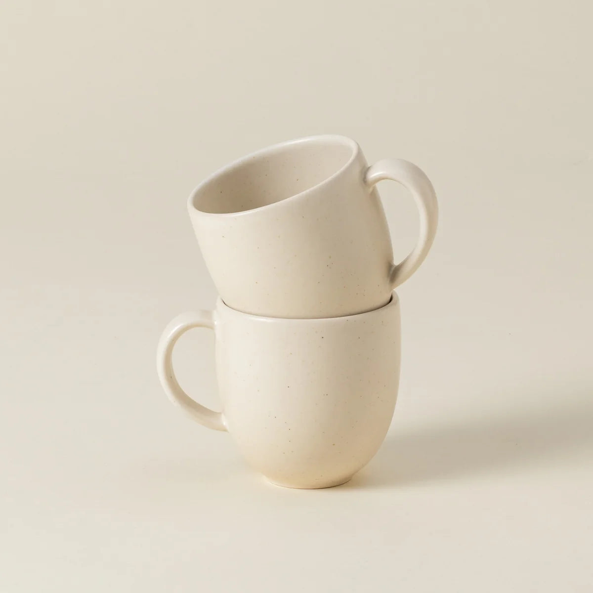 Two Casafina “Pacifica - Vanilla Beige” mugs are stacked, with one mug resting at an angle inside the other on a neutral background.