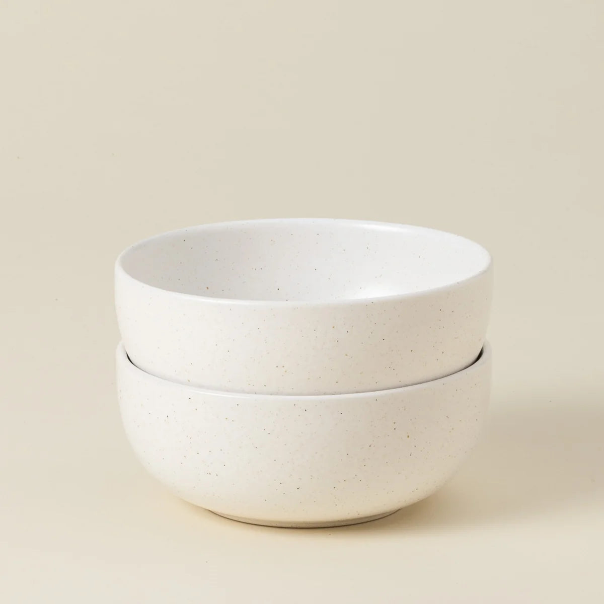 Two stacked Casafina “Pacifica - White” cereal bowls, crafted from smooth, slightly speckled white ceramic, are set against a plain beige background.