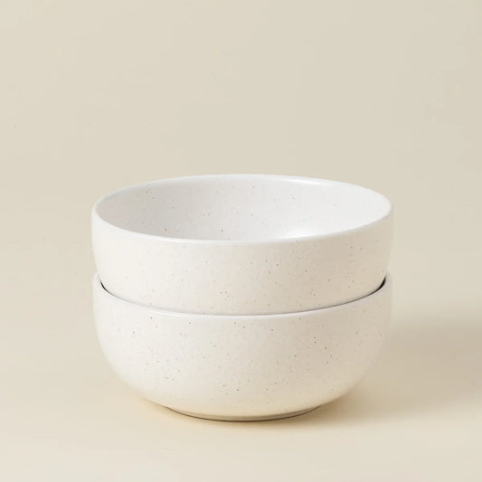 Two stacked Casafina “Pacifica - White” cereal bowls, crafted from smooth, slightly speckled white ceramic, are set against a plain beige background.