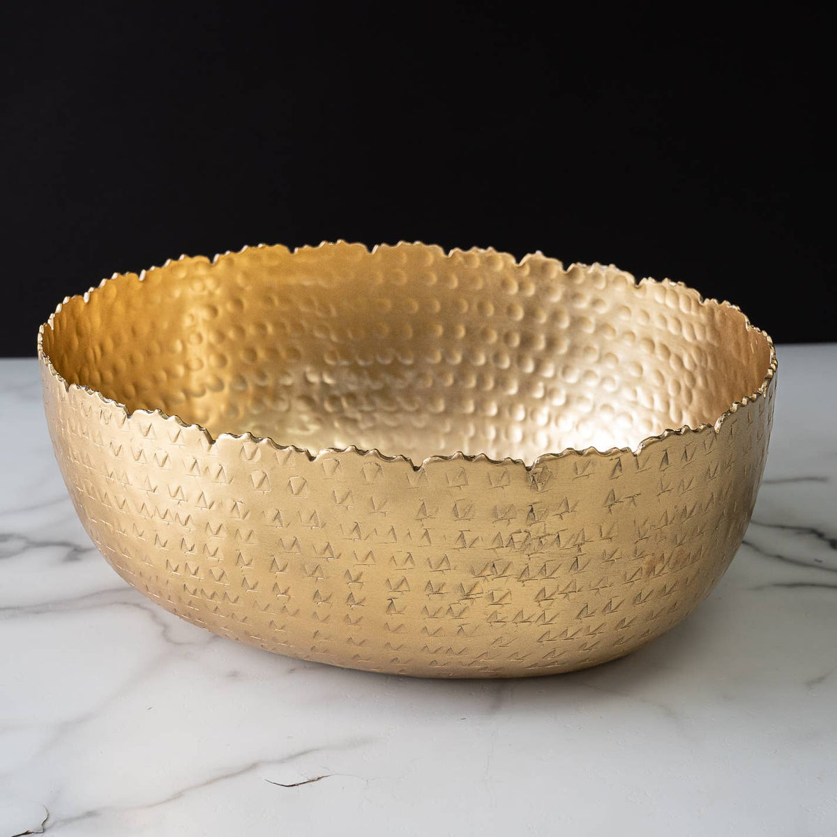India Handicrafts Inc gold oval hammered bowl with textured dimpled surface, front view on marble