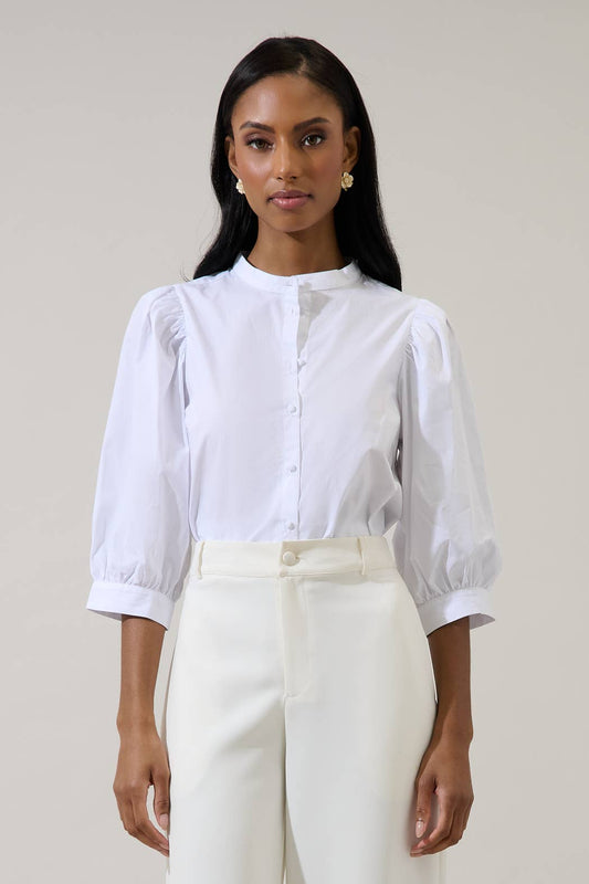 A woman stands facing forward against a plain light background, wearing the Sugarlips Raveny Button Up Puff Sleeve Shirt paired with high-waisted white pants.