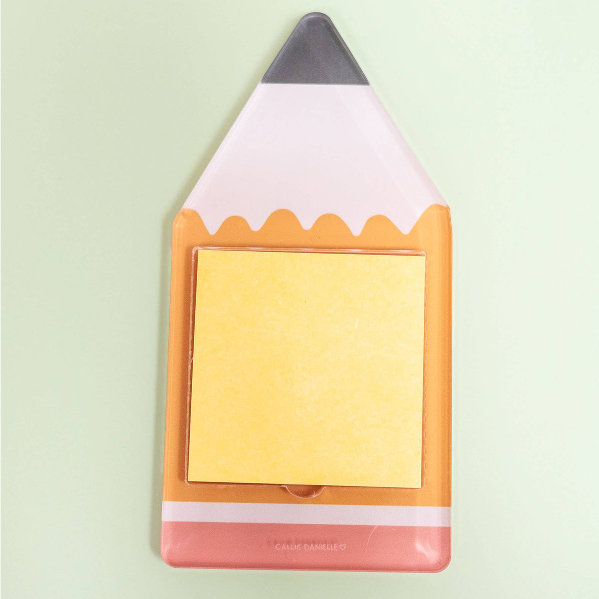 The Callie Danielle - Pencil Sticky Note Holder by Callie Danielle, featuring a stack of yellow sticky notes and a fun pencil-shaped design, sits on a light green background—making it the perfect back-to-school gift.
