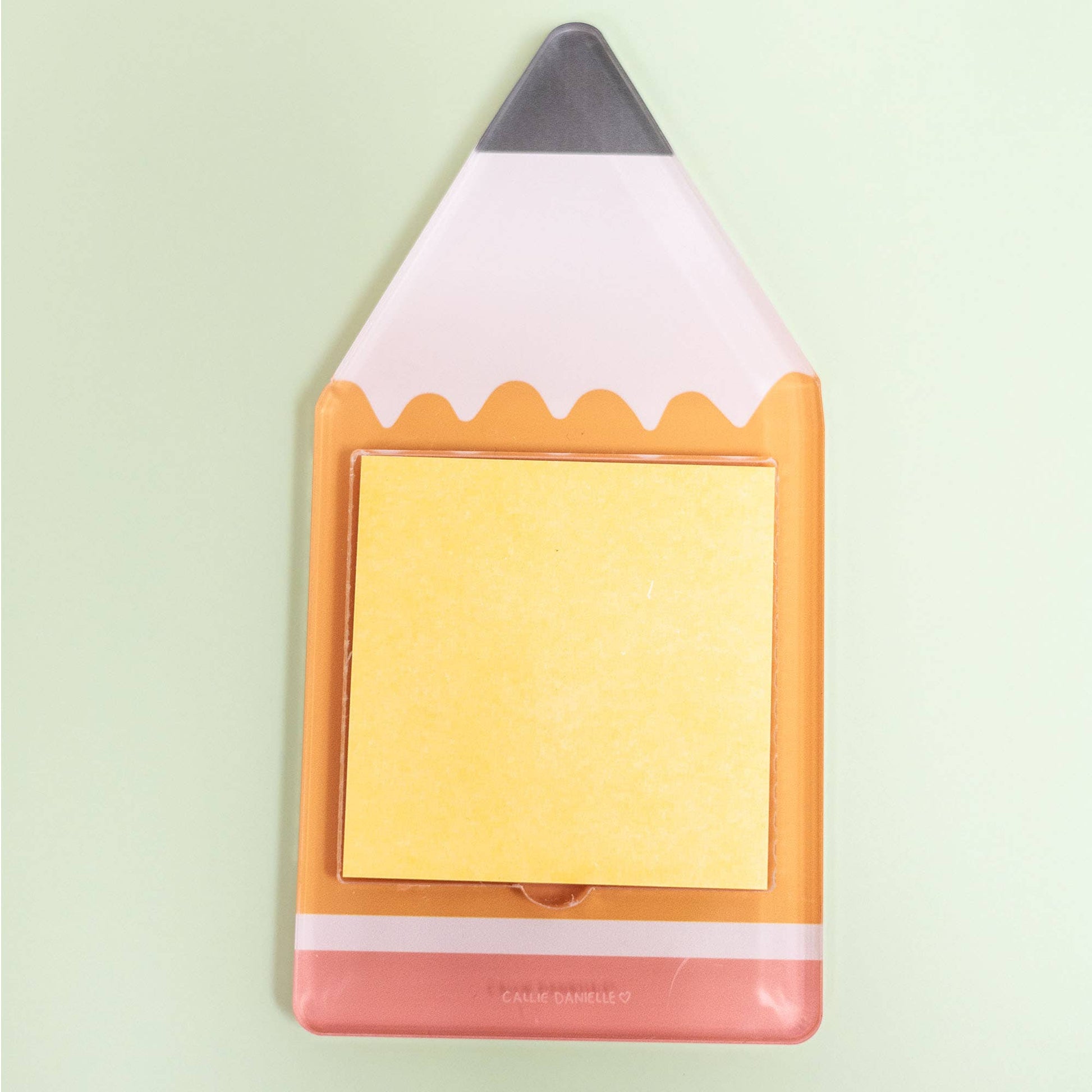 The Callie Danielle - Pencil Sticky Note Holder by Callie Danielle, featuring a stack of yellow sticky notes and a fun pencil-shaped design, sits on a light green background—making it the perfect back-to-school gift.