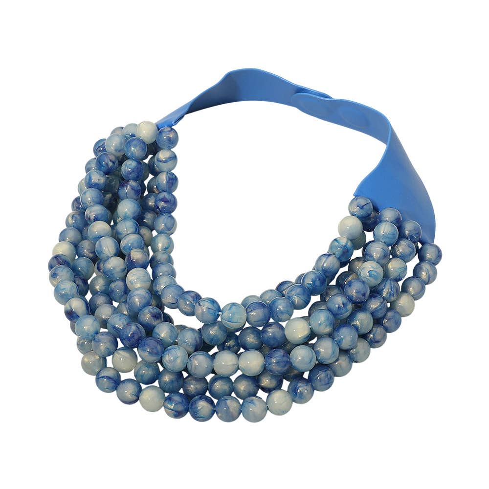 The Sensibling Corp. Marbled Ball Beaded Multi Layered Faux Leather Magnetic Collar Necklace features multiple strands of blue and white marbled beads attached to a wide blue faux leather band, making this layered statement piece a bold and sophisticated addition to any outfit.