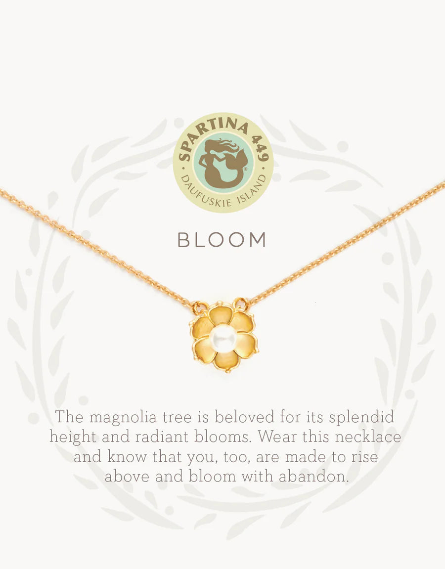 The Spartina Sea La Vie Bloom Necklace features a gold magnolia flower pendant on a delicate chain, displayed above the word "BLOOM" and an uplifting message about the magnolia tree's beauty and symbolism of rising above. This inspirational jewelry piece from Spartina captures both elegance and meaningful encouragement—a beautiful magnolia necklace designed to remind you to shine. The Spartina logo appears at the top.
