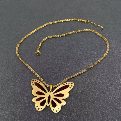 Introducing the Mio Queena - Dried Flower Brass Butterfly 18K Golden SS Necklace - PDF by Mio Queena, a gold-plated chain necklace adorned with a butterfly-shaped pendant featuring exquisite cutout details and delicate dried flowers. Displayed on a dark textured surface, this piece seamlessly combines timeless elegance with modern artistry, making it a stunning addition to any jewelry collection.