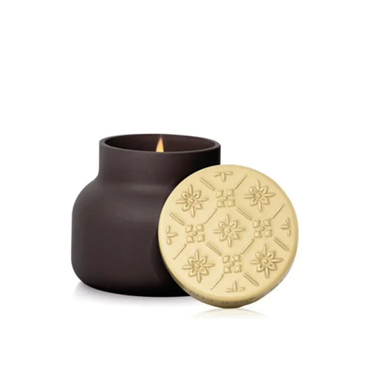Capri Blue Artisan Terrazza Velluto Signature Candle 19oz in charcoal gray with gold patterned lid beside vessel