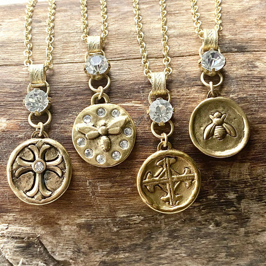 Four VB&CO Designs gold pendant necklaces with crystal stones: cross, bee, ornate cross, and bee medallion charms