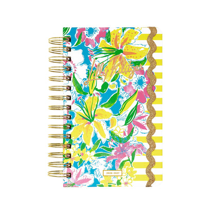 Certainly! Here is your rewritten sentence using the provided product data: The Lilly Pulitzer by Lifeguard Press - Medium 17 Month Agenda in the Lovely Lilly print features a colorful spiral-bound design adorned with yellow, pink, and blue floral patterns, cheerful yellow and white stripes, and a gold glitter scalloped border on the cover. This vibrant 2026–2027 agenda displays the year at the bottom, making it a stylish and practical choice for staying organized.
