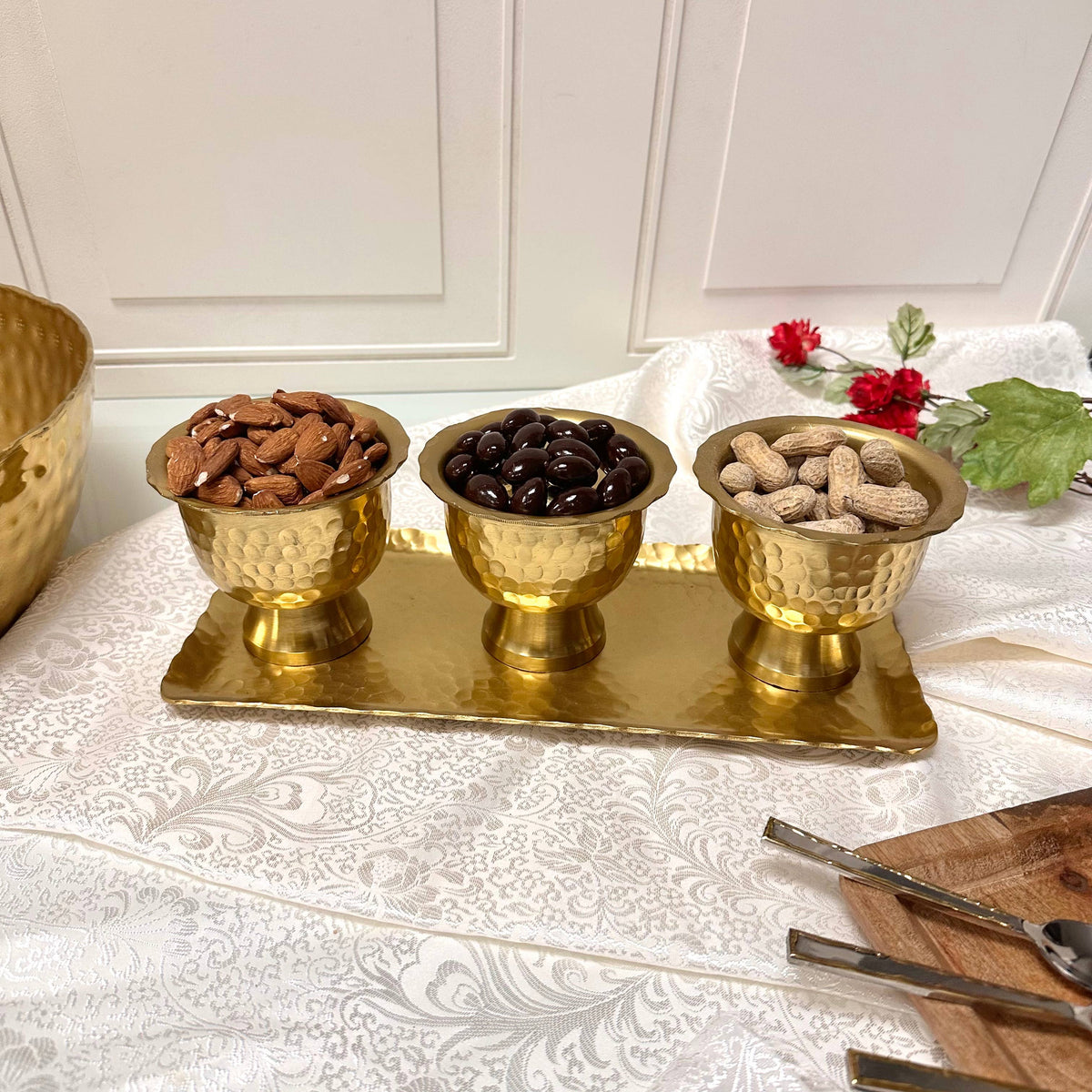 Gold pedestal bowls filled with almonds, olives, and peanuts on brass tray, styled display
