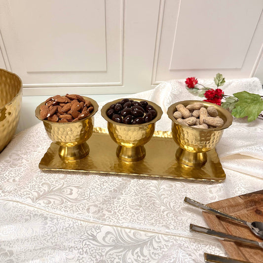 Gold pedestal bowls filled with almonds, olives, and peanuts on brass tray, styled display
