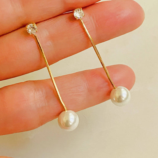 Ellison+Young Dangling Pearl Earrings held in hand showing gold chain with crystal stud and pearl drop