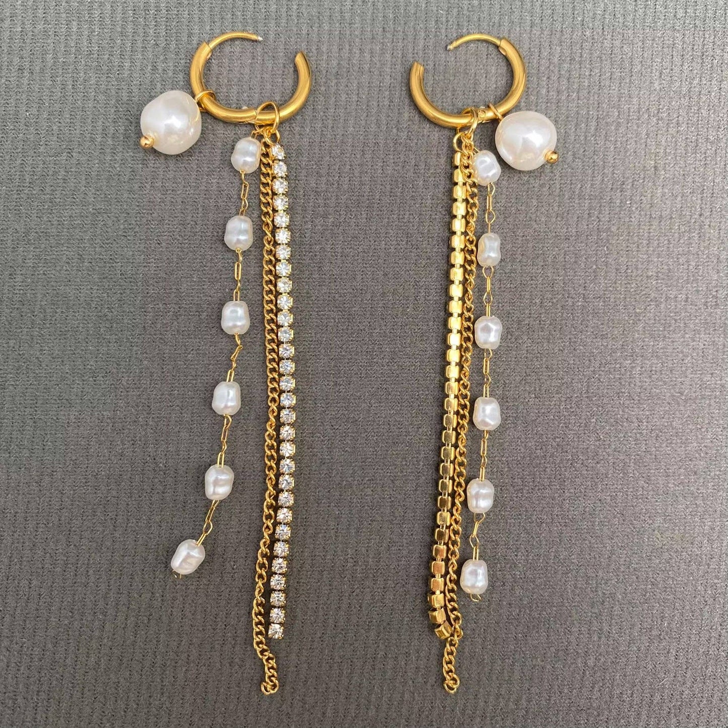 Mio Queena's Zircon & Pearl Fringe 18K Gold Plated SS Huggie Earrings-FGS feature elegant hoop designs embellished with pearl studs, delicate gold chains—one set with shimmering zircons—and strings of petite white pearls, all beautifully displayed on a gray textured background. These hypoallergenic earrings offer a perfect blend of sophistication and comfort for everyday wear.